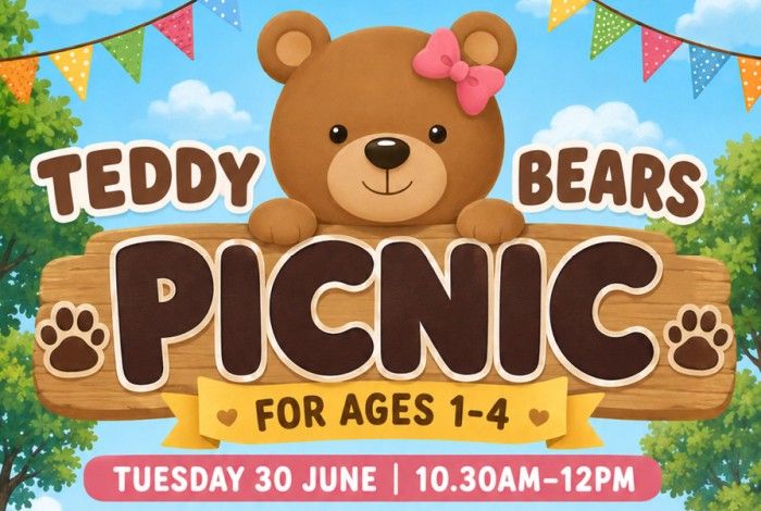 A colourful children's event graphic featuring a smiling teddy bear peeking over a large wooden sign that reads “Teddy Bears Picnic.” The bear has a pink bow on one ear, and the scene is set outdoors with green trees, a bright blue sky, fluffy clouds, and colourful bunting flags hanging across the top. A yellow ribbon below the sign states “For Ages 1–4,” and a pink banner at the bottom displays the event date and time: “Tuesday 30 June | 10.30am–12pm.”